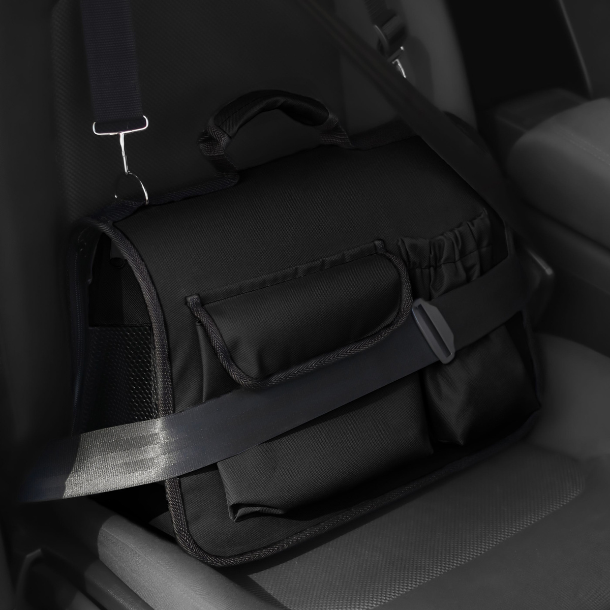 Серая сумка-переноска для животных стоит на пассажирском сиденье и пристегнута ремнем безопасности.