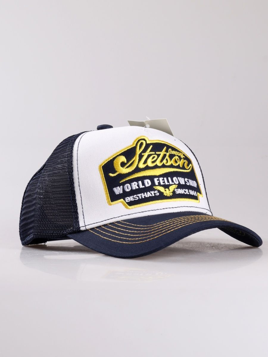 TRUCKER CAP AMERICAN HERITAGE от культового американского бренда Stetson. Тракерами бейсболки с сеточкой назвали в честь дальнобойщиков, которые носили такие головные уборы не только на работе, но и в повседневной жизни. Бейсболка выполнена из чистого хлопка тёмно синего цвета и прошита желтой и синей строчками. На передней панели – патч с вышитыми надписями STETSON world fellowship («всемирное братство»), Best hats since 1865 («Лучшие головные уборы с 1865 года»).